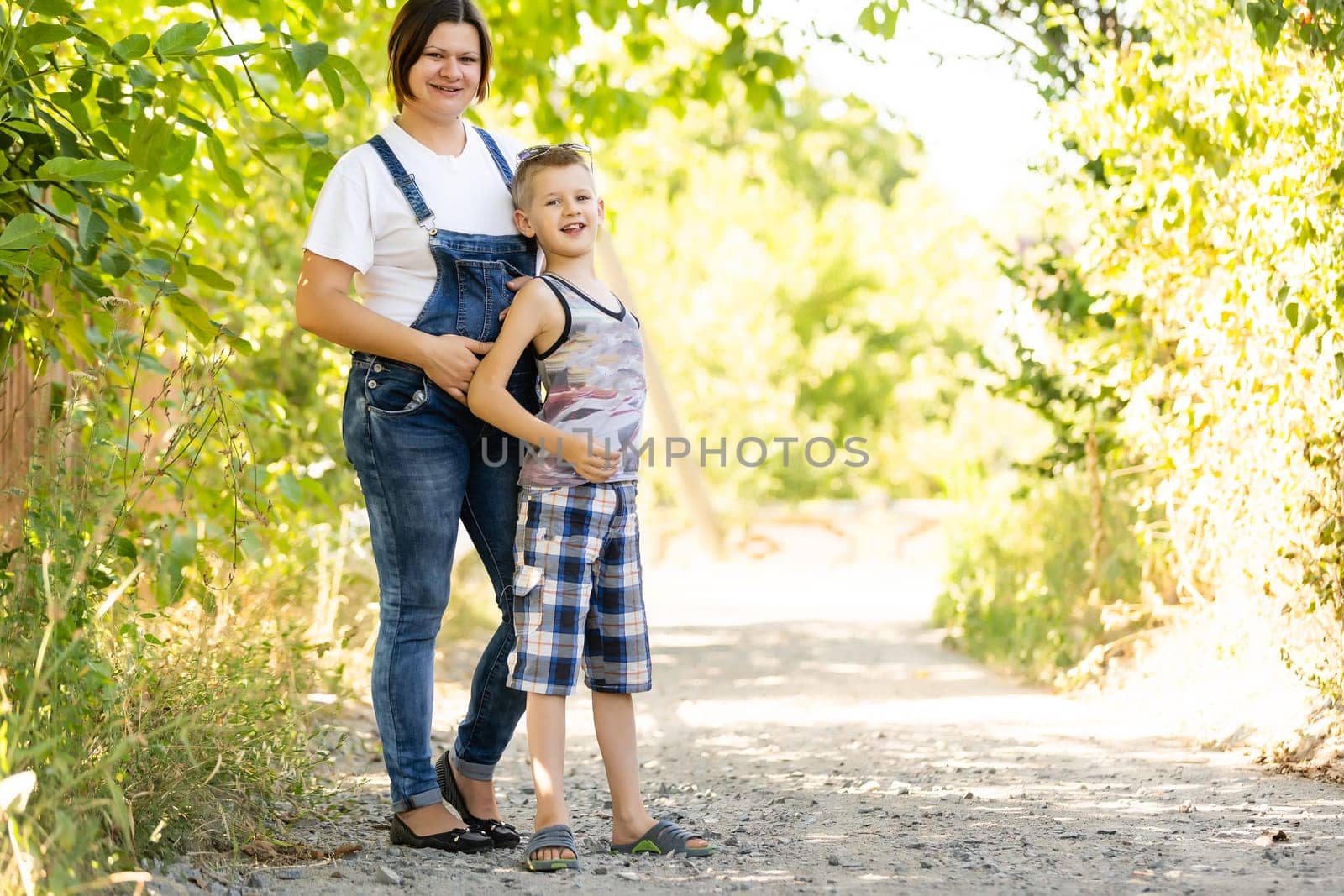 Pregnant woman walking countryside with her son. Child hugging his pregnant mother.
