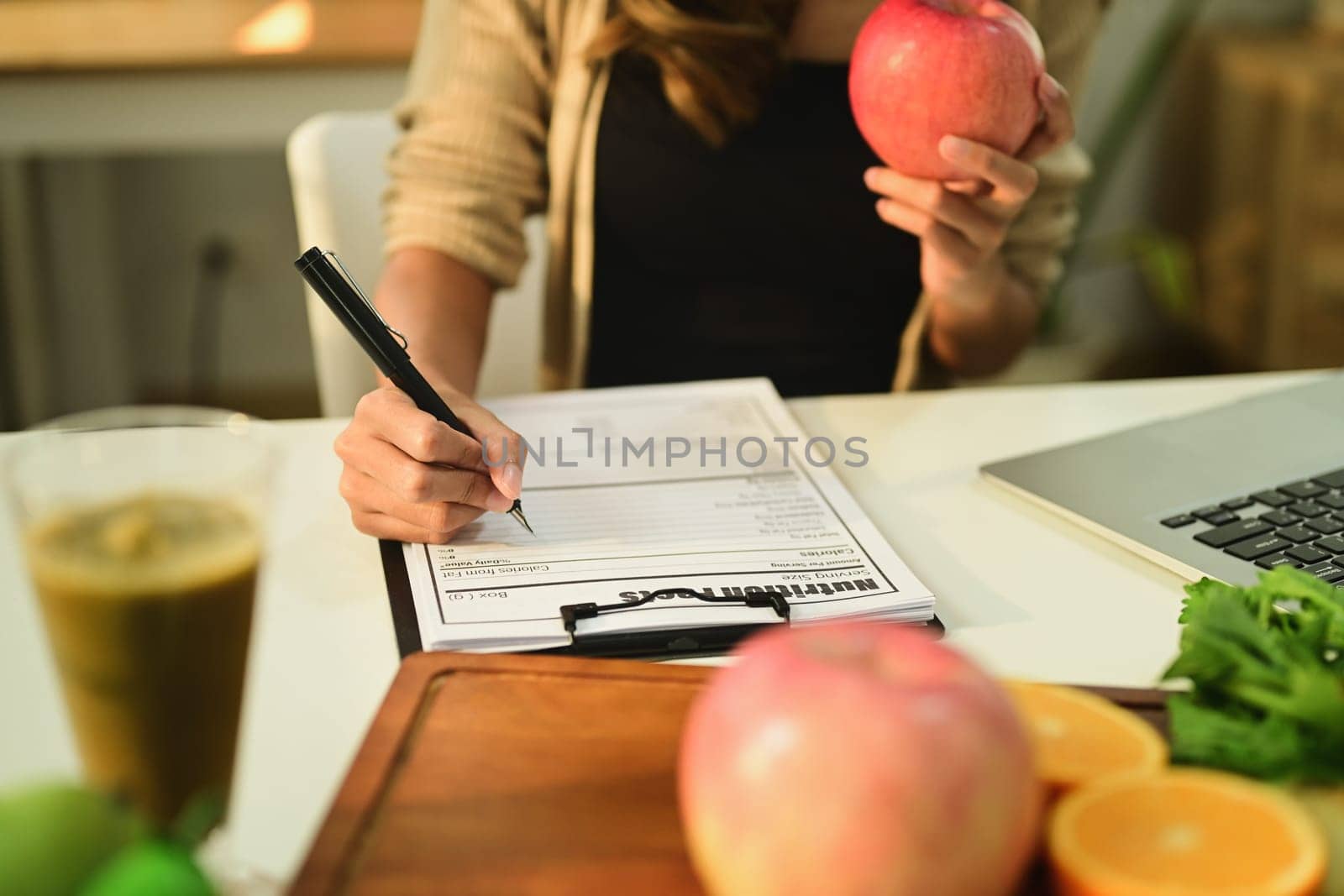 Nutritionist holding an apple and writing recipe at working desk with fresh fruit. Healthcare and diet concept by prathanchorruangsak