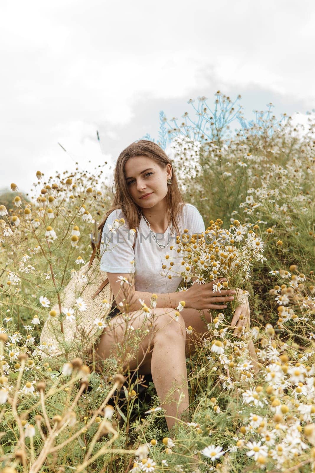 Beautiful young woman in nature with a bouquet of daisies. Field daisies, field of flowers. Summer tender photo.