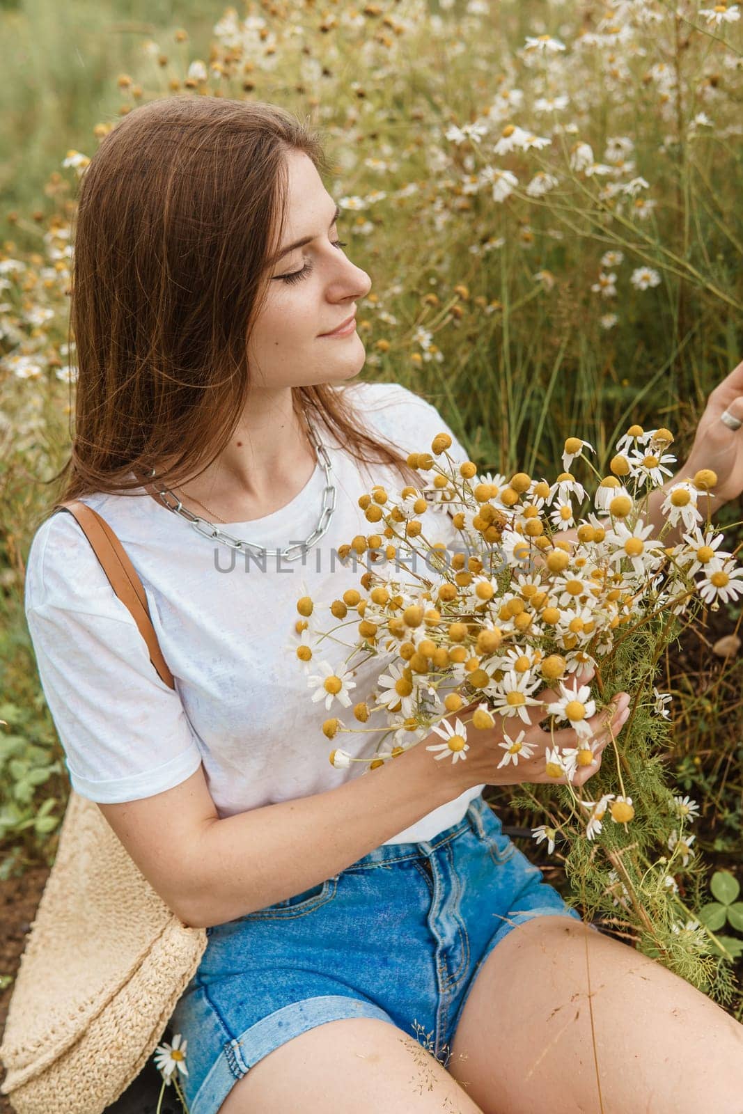 Beautiful young woman in nature with a bouquet of daisies. Field daisies, field of flowers. Summer tender photo.