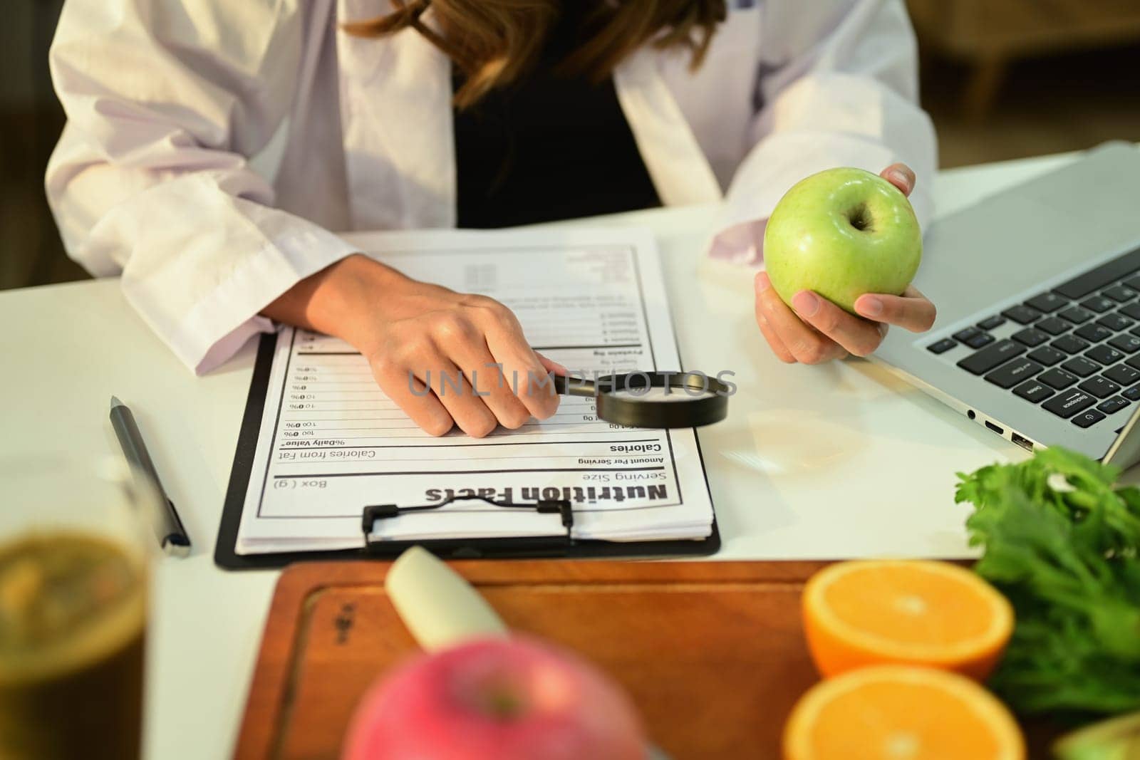 Cropped image of nutritionist holding an apple and prescribing recipe at desk with fresh fruit. Healthcare and diet concept by prathanchorruangsak