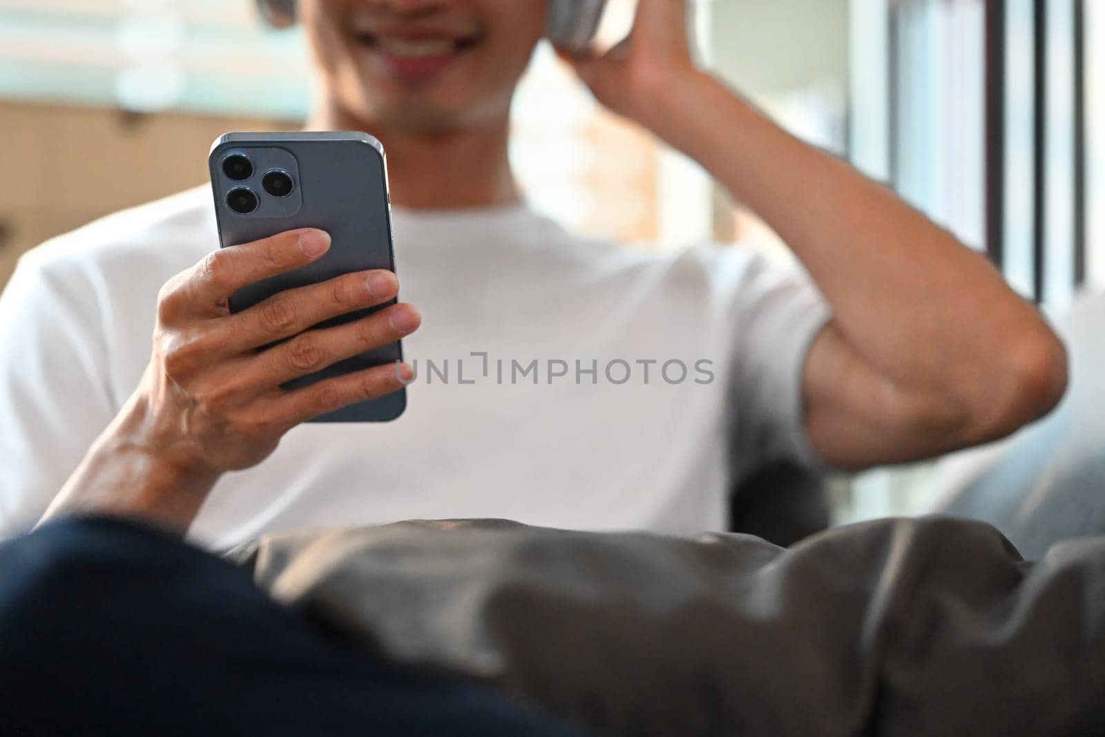Selective focus on hand. Smiling man using smart phone and relaxing on couch. People, Technology and lifestyle concept.