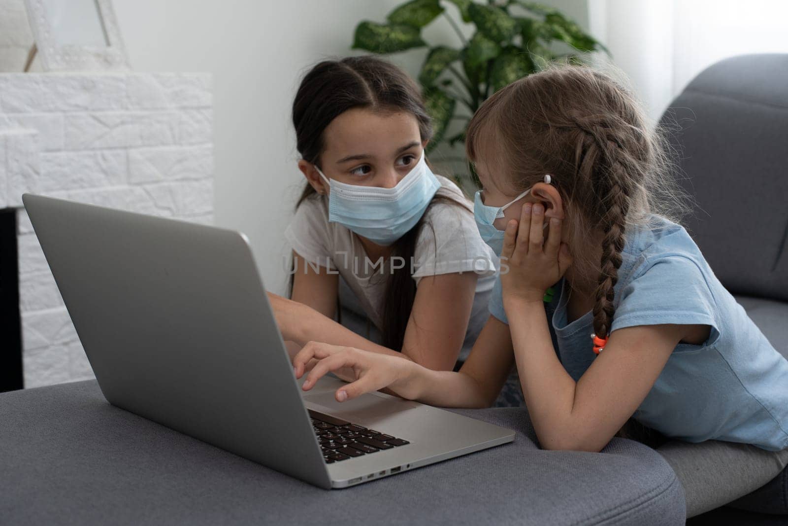 Happy two little child girl learning, studying online and working on laptop with face mask.