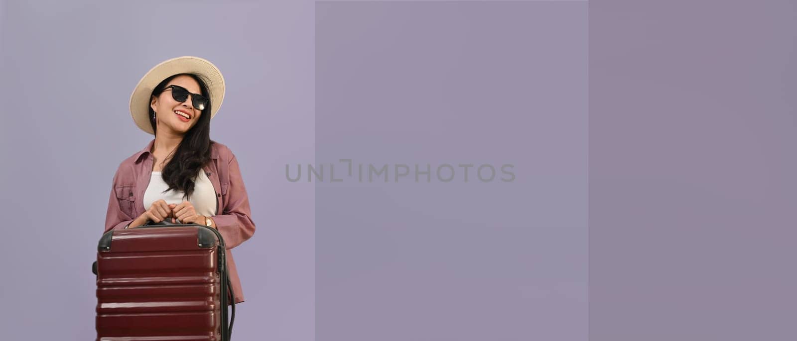 Elegant beautiful woman dressed in summer clothes with luggage isolated purple background with copy space for your graphic design.