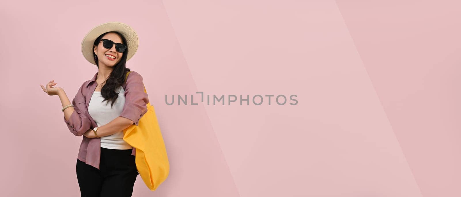 Confident woman wearing summer clothes, hat and sunglasses isolated over pink background with copy space for graphic design by prathanchorruangsak