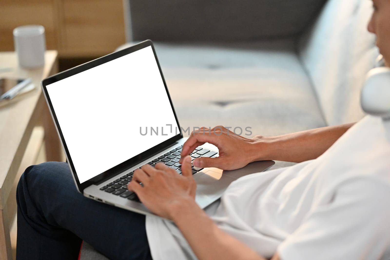 Close up view of casual man browsing internet on laptop, resting on couch in bright living room.