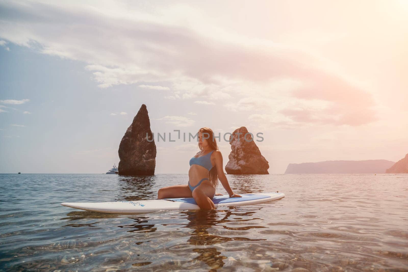 Close up shot of beautiful young caucasian woman with black hair and freckles looking at camera and smiling. Cute woman portrait in a pink bikini posing on a volcanic rock high above the sea