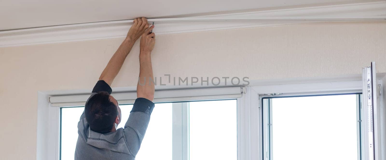 A handyman installing new cornice for curtains, home repair and renovation works by Andelov13