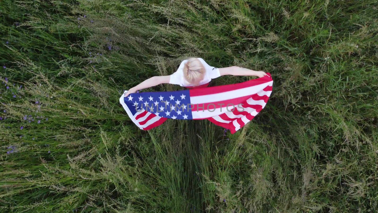 full length blond Woman holding American Flag in trees shadow of sunlight Back view cute blondy girl run on fresh green grass texture.