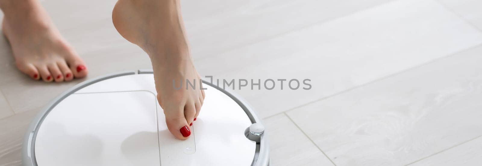 Human leg using smart robotic technology vacuum cleaner cleaning floor tiles background. Closeup top view image by Andelov13