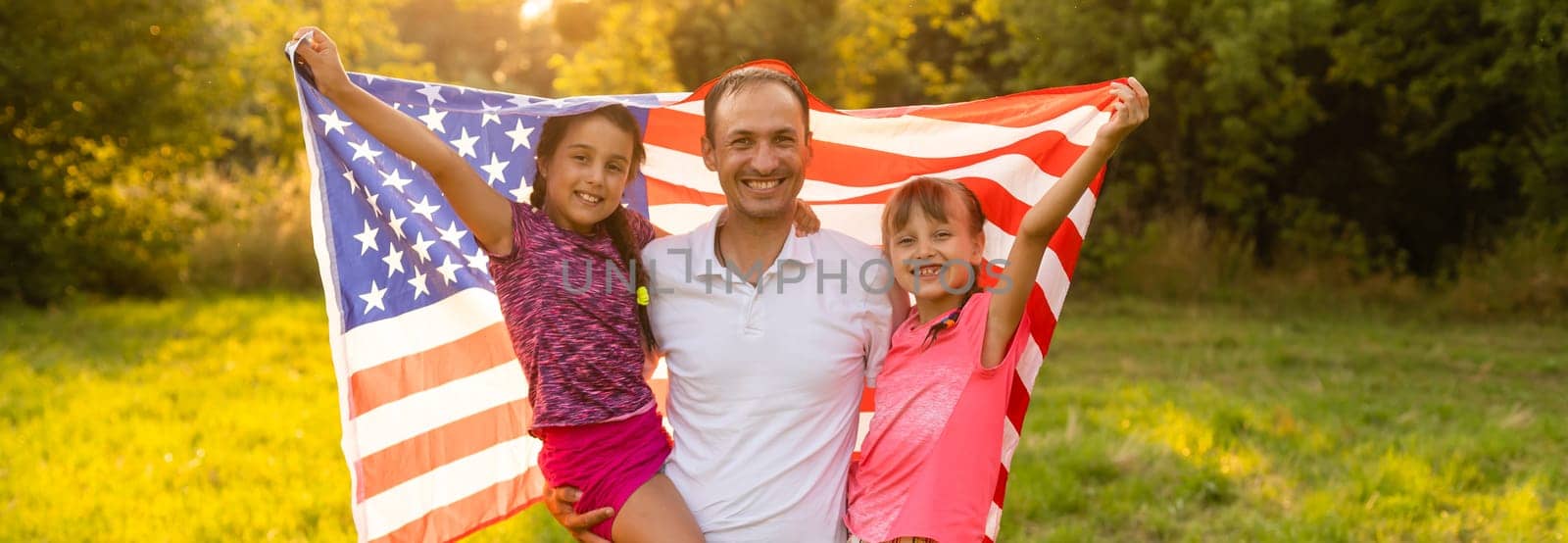 parents and child with American flag are playing with a colorful kite. mother, father and their little daughters celebrate together 4th of July outdoors in foggy day. Independence Day of USA concept