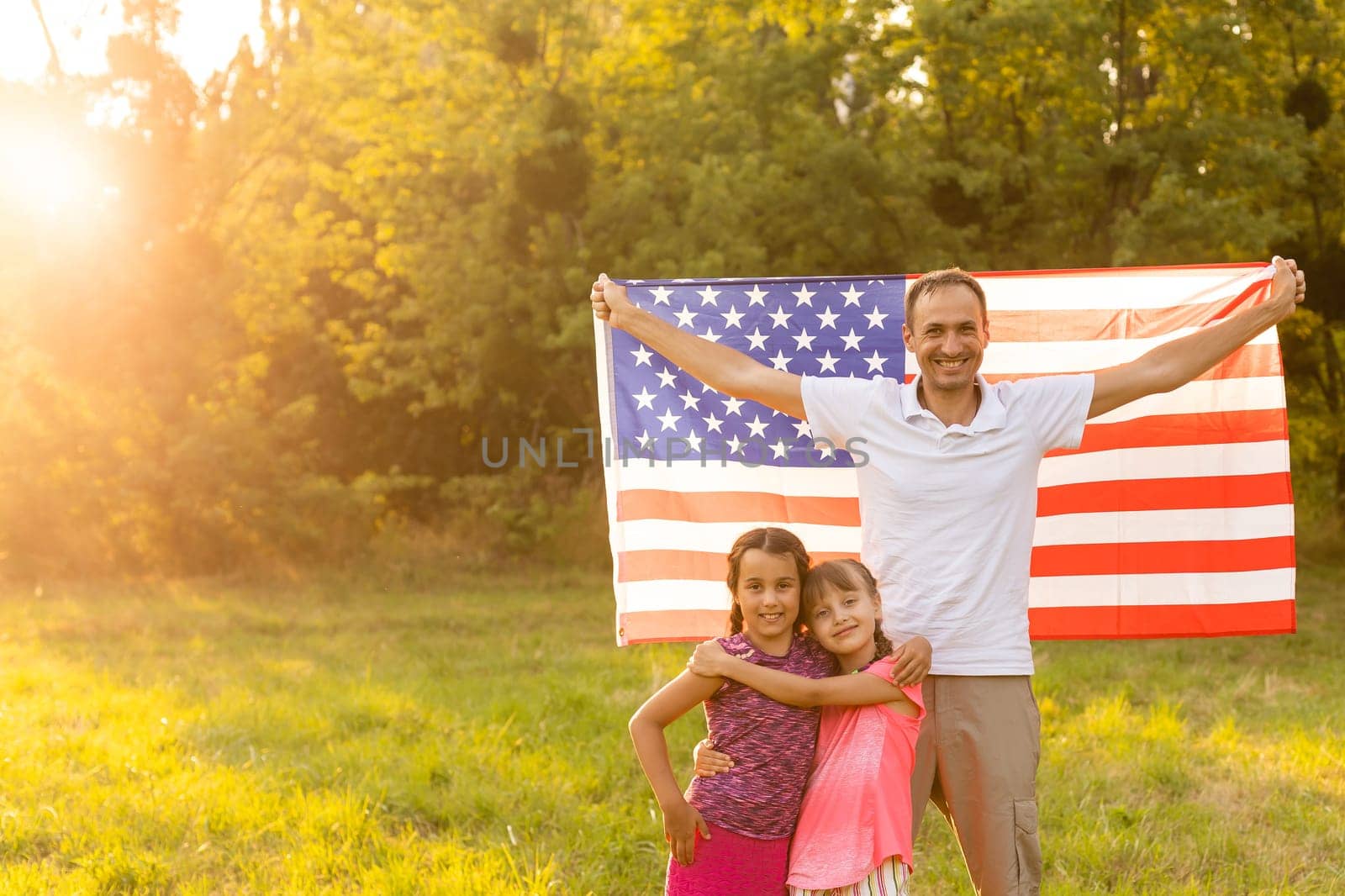 parents and child with American flag are playing with a colorful kite. mother, father and their little daughters celebrate together 4th of July outdoors in foggy day. Independence Day of USA concept