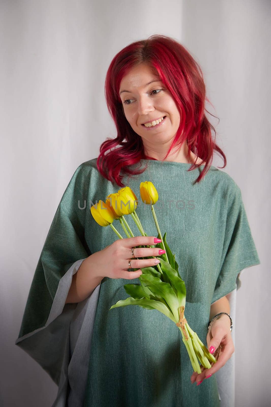 Beautiful woman with red hair in yellow dress on a light background holds tulips. Inernational woman's day 8 March by keleny