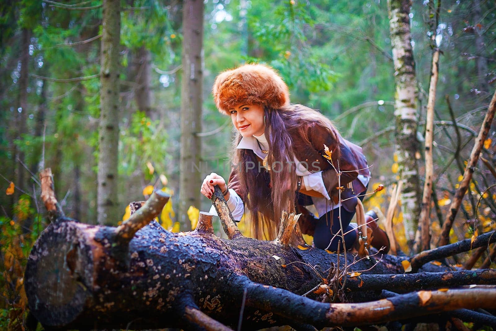 Girl in a leather jacket, a big red fox fur hat in the forest in autumn. A female model poses as a fabulous royal huntress on nature hunt at a photo shoot