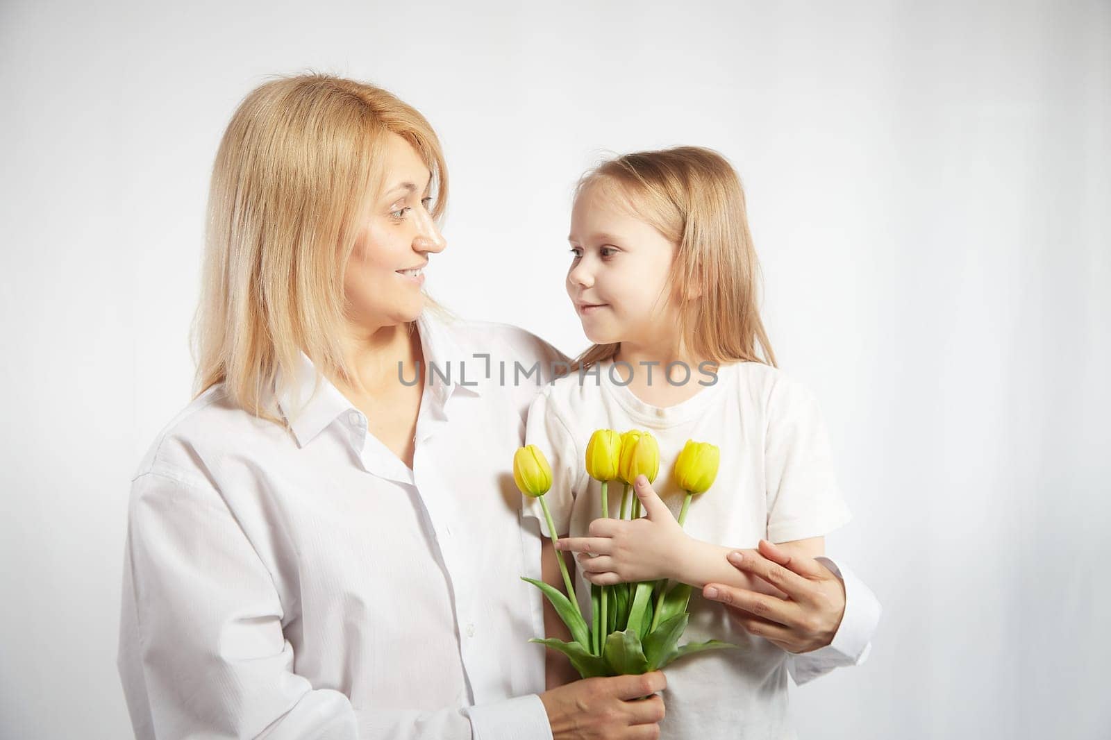 Blonde mother and daughter with a bouquet of tulips on a white background. Mom and girl together on holiday mother's day with flowers. Congratulations to women on International Women's Day on March 8