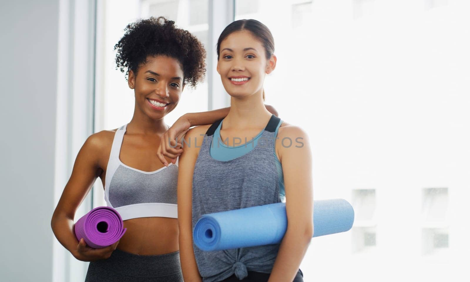Lets get our yoga on. Cropped portrait of two attractive young women standing and holding yoga mats and posing before working out indoors. by YuriArcurs