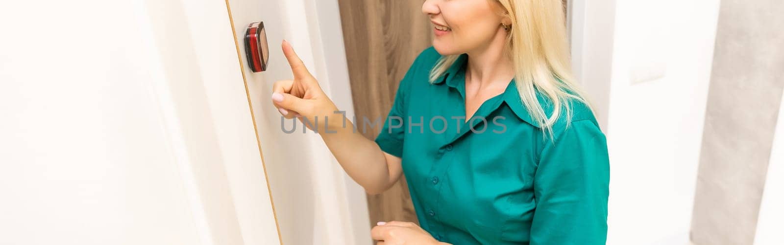 A woman is pressing the up button of a wall attached house thermostat with digital display showing the temperature. A concept image for electricity bill, heating, cooling, eco friendly, saving etc.