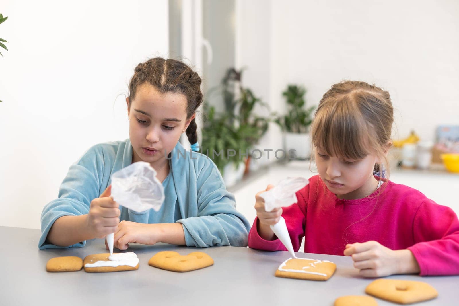 two beautiful sisters decorate and eat delicious cakes at a wooden table.