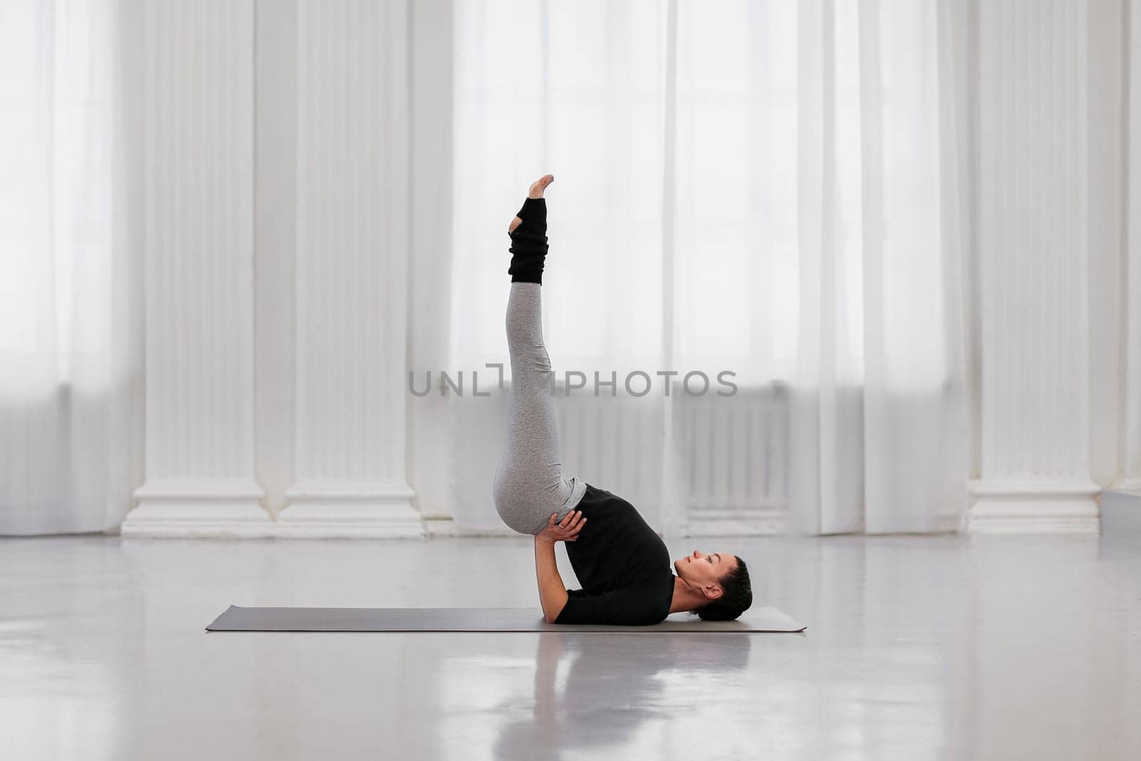 Professional instructor young woman does sarvangasana during a yoga class in a white light studio. The concept of getting rid of any ailment from allergies to nervous tension by apavlin
