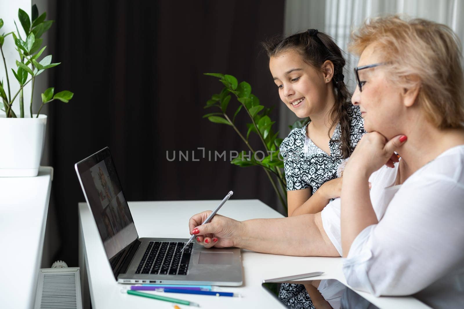 Happy grandmother and her granddaughter having video chat via laptop together at home