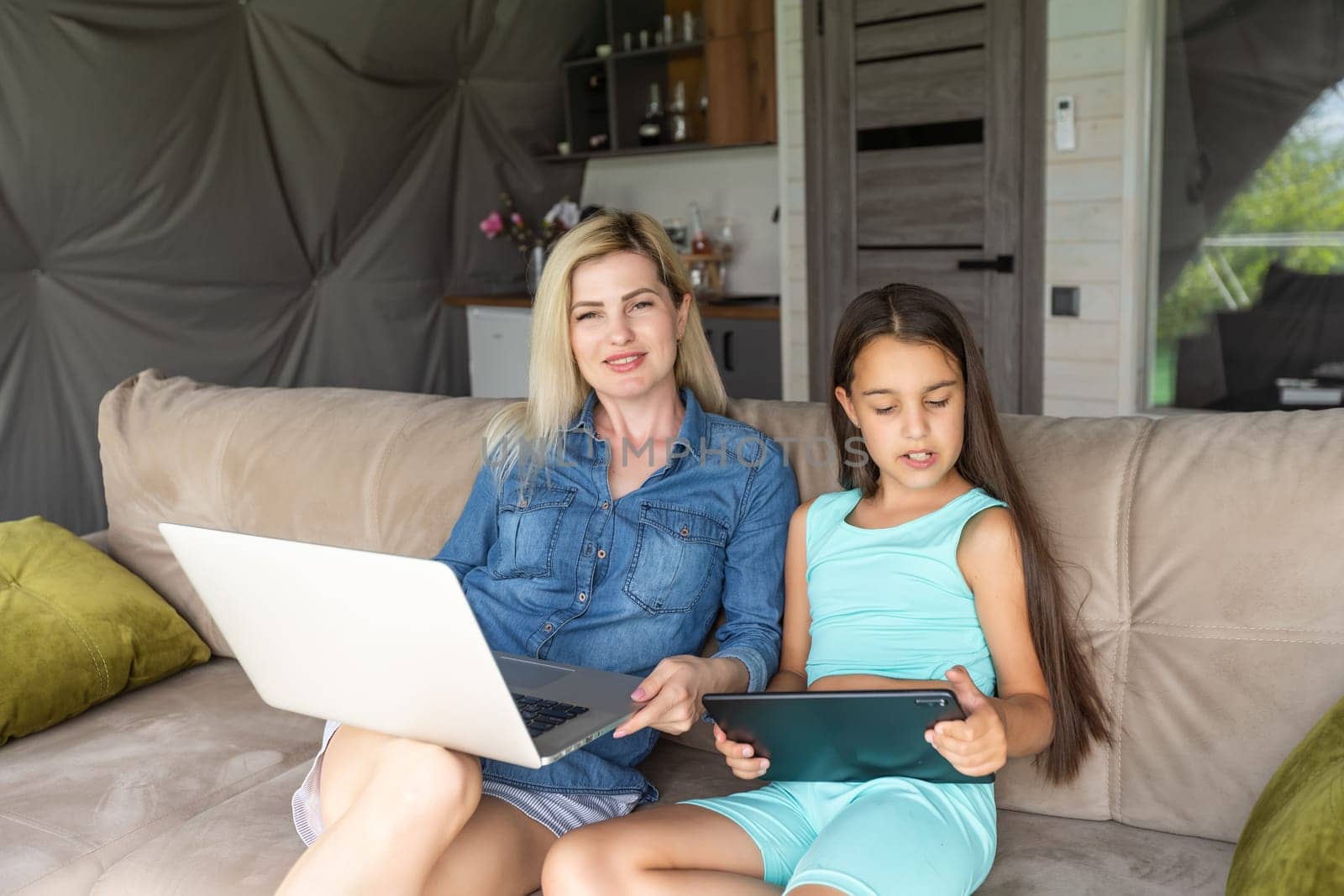 mother and daughter with laptop and tablet on sofa.