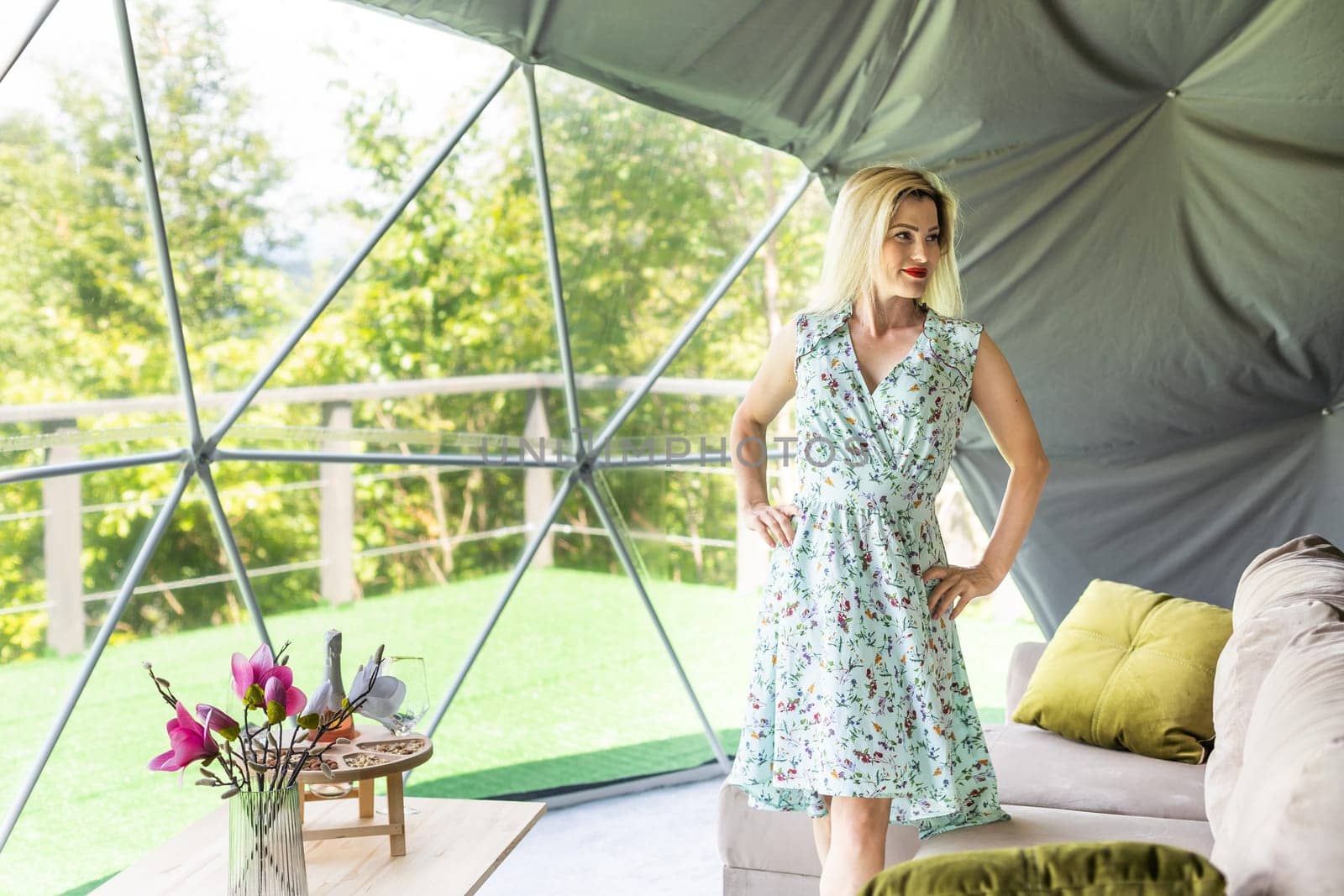 Woman looking out at nature from geo dome tents. Green, blue, orange background. Cozy, camping, glamping, holiday, vacation lifestyle concept. Outdoors cabin with scenic background