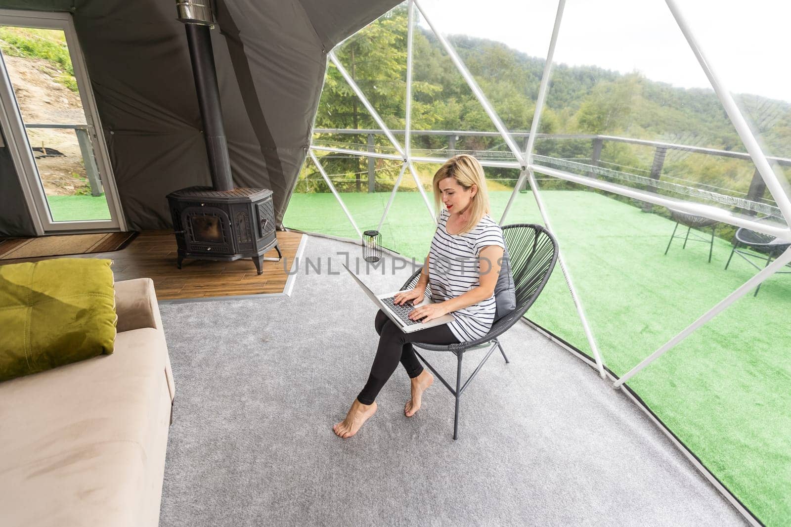 Transparent bubble tent at glamping, Lush forest around and interior. Woman with laptop.