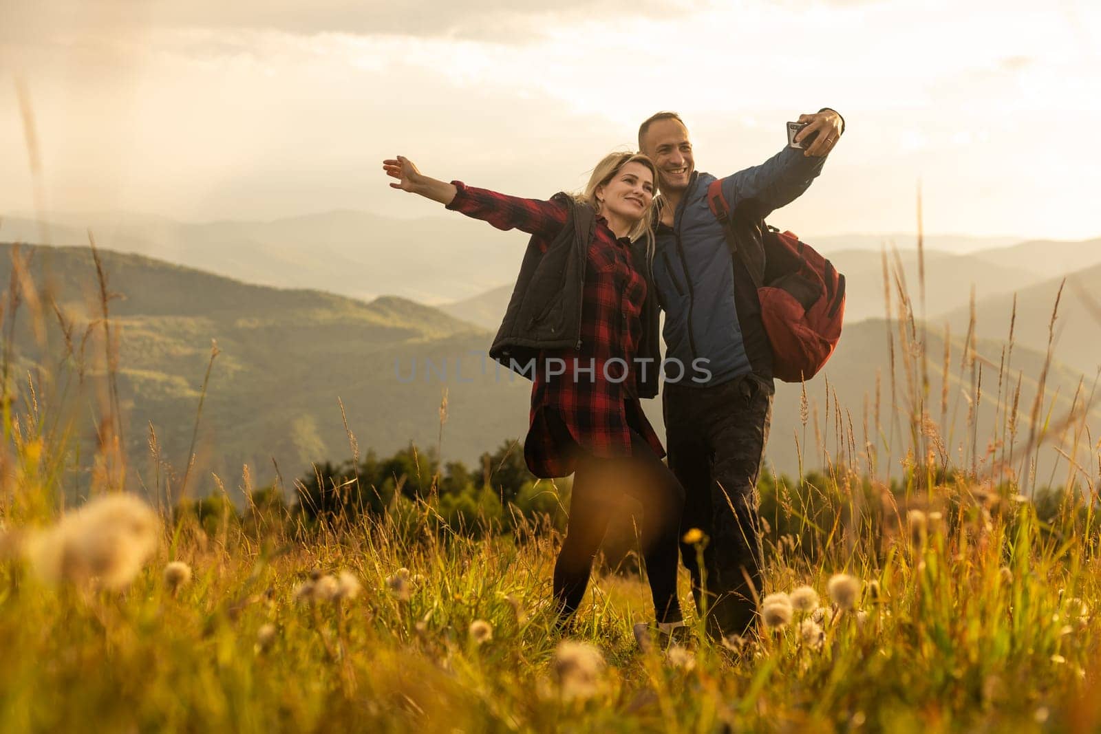 A man and a woman in tourist equipment are standing on a rock and admiring the panoramic view. A couple in love on a rock admires the beautiful views. A couple in love is traveling. A couple on a hike