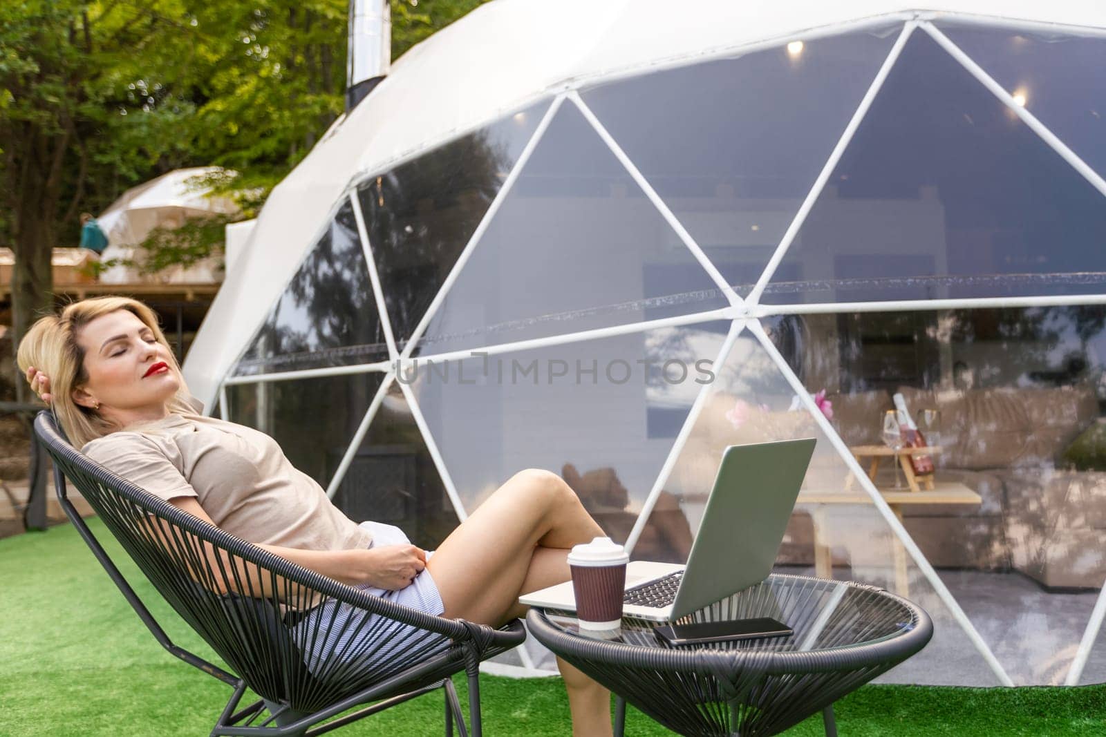 Positive woman chatting on laptop and and looking at screen near dome geometric structure.