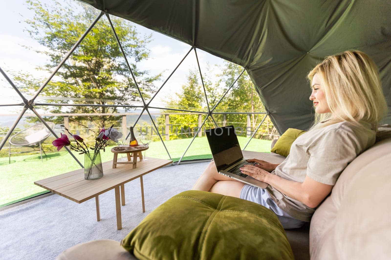 middle aged woman uses a laptop resting and spending time at Glamping house on holidays. holiday dome tent. Cozy, camping, hygge, lifestyle concept.