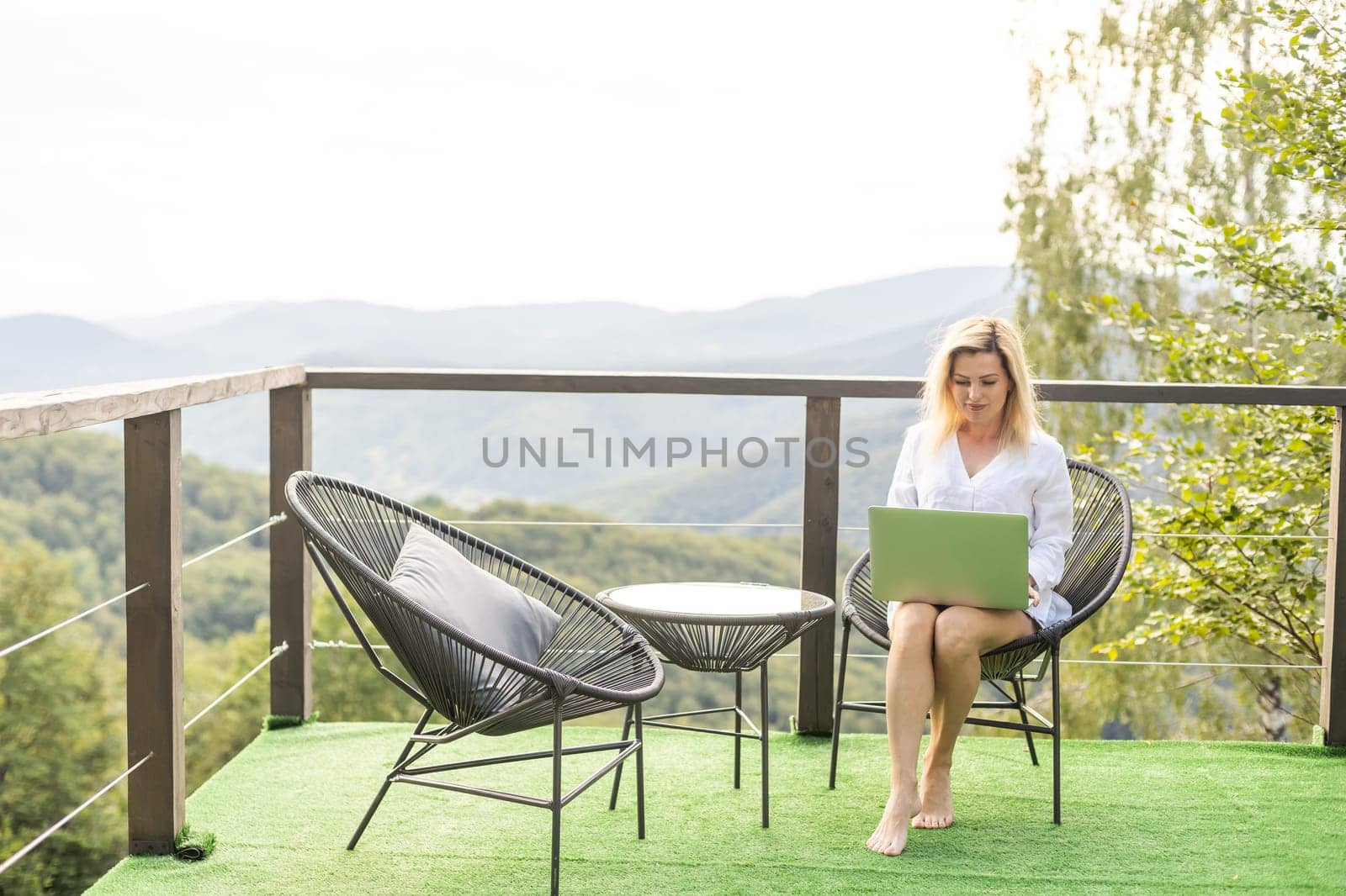 a woman with a laptop on a terrace in the mountains.