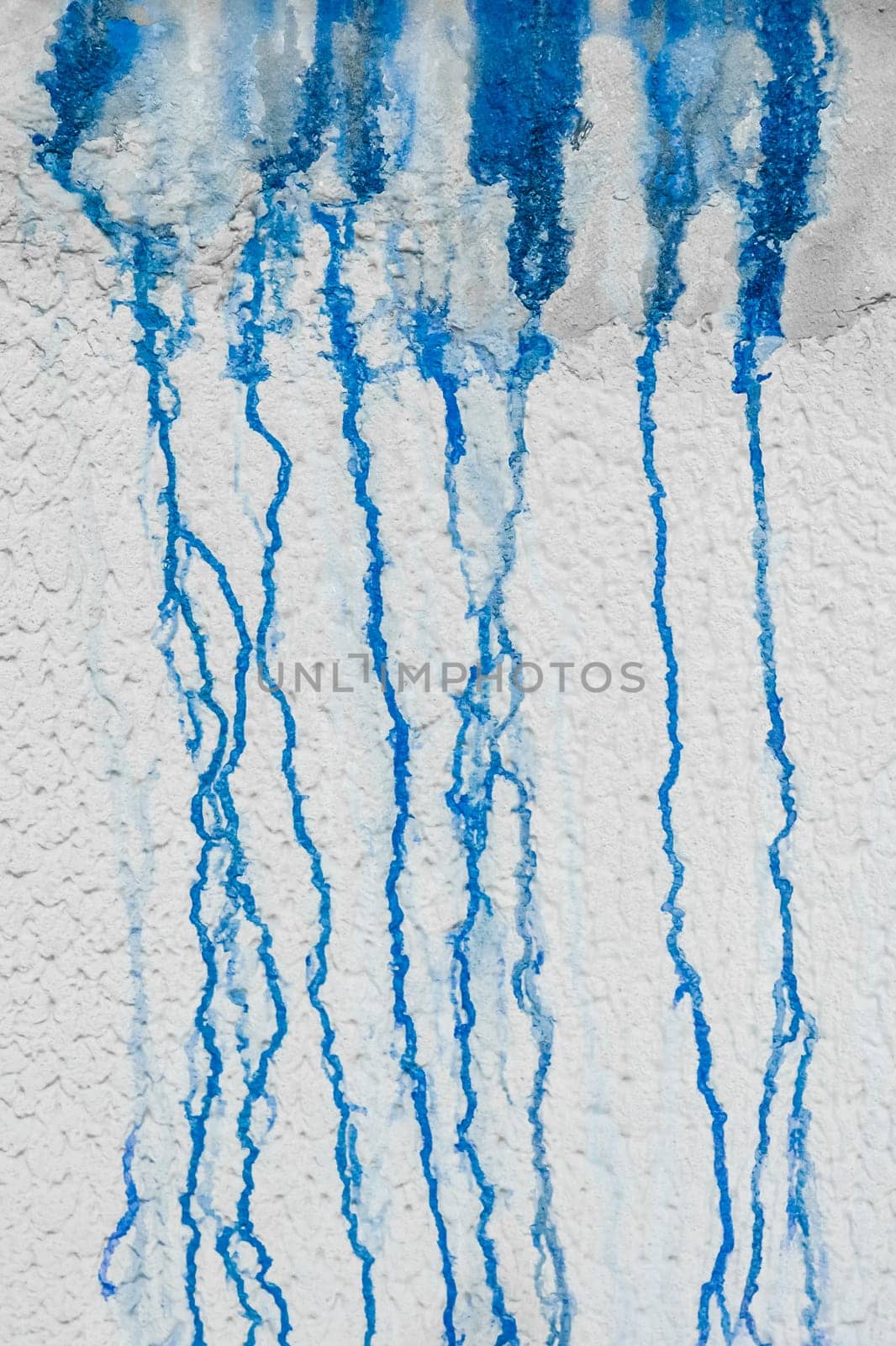 Streaks of liquid spilled blue paint down the white plaster wall abstract pattern dirty background design.