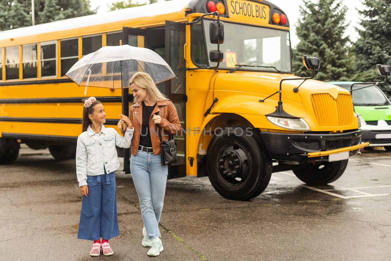 Back to school. Pupils of primary school near school bus. Happy children ready to study. little girl with mom going to bus by Andelov13