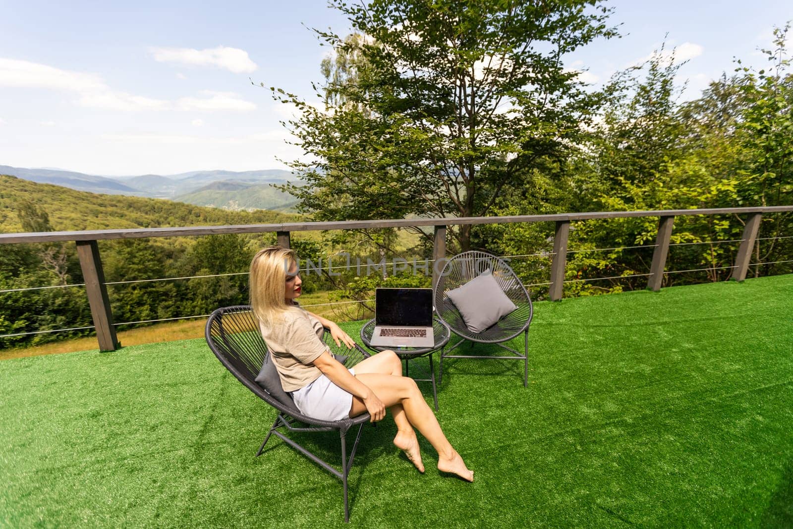 woman sitting on hotel balcony with laptop computer while working remote on freelance. mountains view.