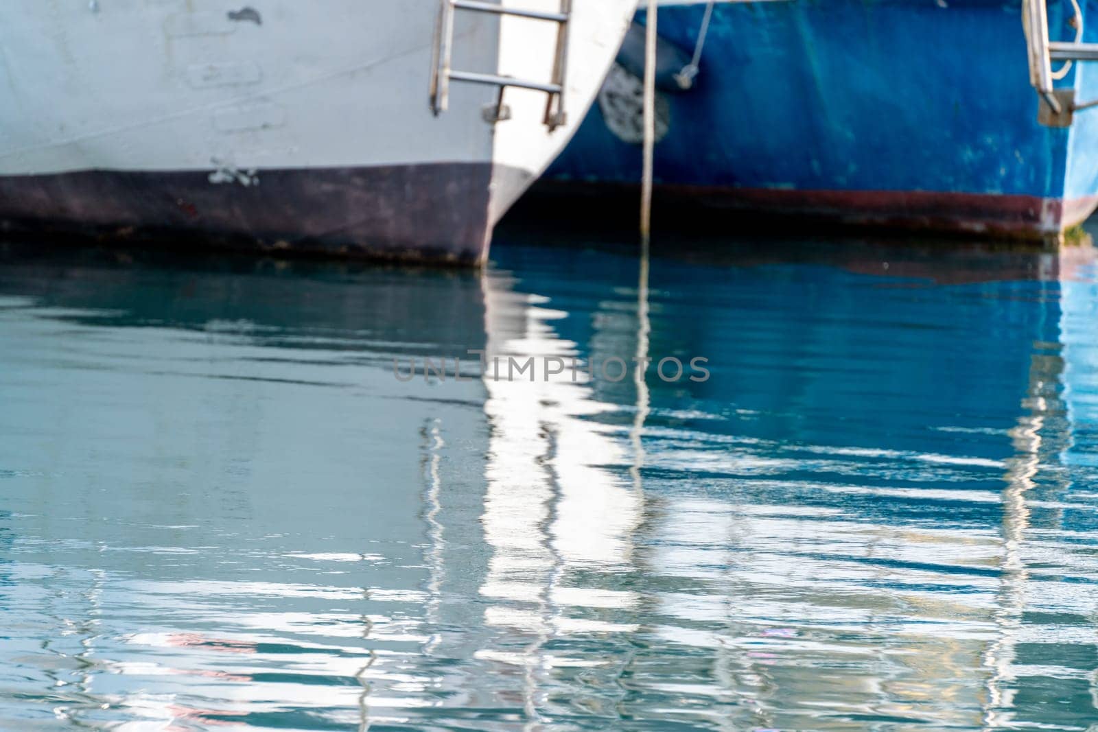 Reflection in the sea surface of white yachts parked in the port on the shore. Fragment of a ship on the water and the reflection of ships in the sea. motionless mirrored water of the sea.
