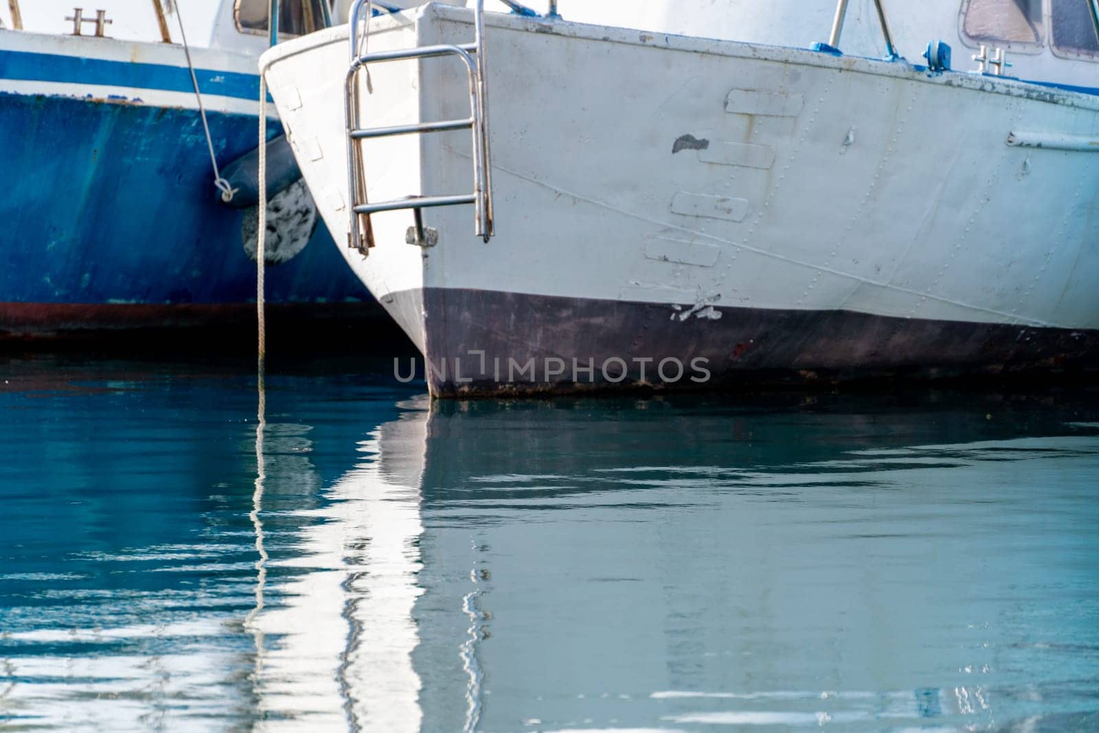 Reflection in the sea surface of white yachts parked in the port on the shore. Fragment of a ship on the water and the reflection of ships in the sea. motionless mirrored water of the sea.
