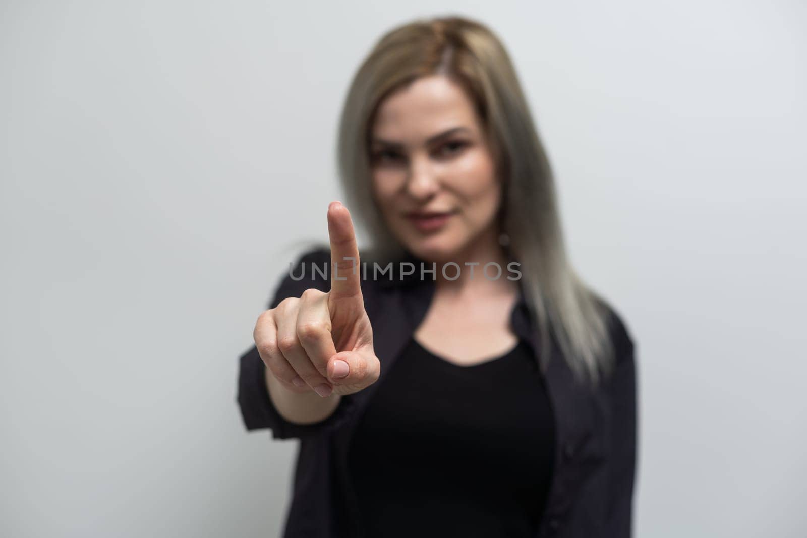 Studio shot of a young blond woman pointing towards you.
