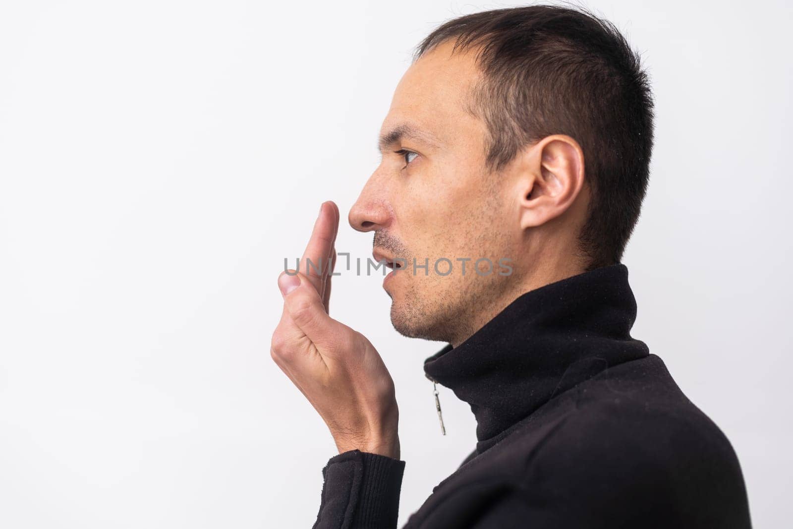 Bad breath. The concept of halitosis. A young man checks his breath with his hand.