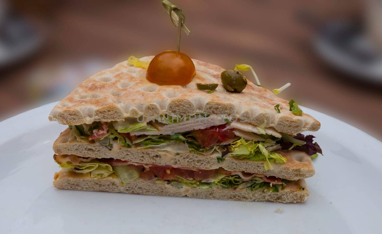 sandwich on a plate served with tomato olive lettuce bacon chicken and fresh lettuce on a bread