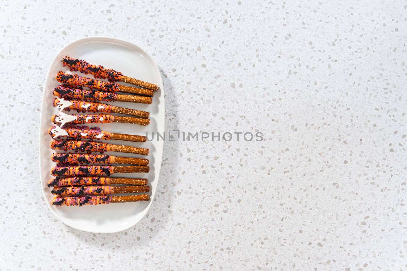 Flat lay. Halloween chocolate-covered pretzel rods with sprinkles on a white serving plate.
