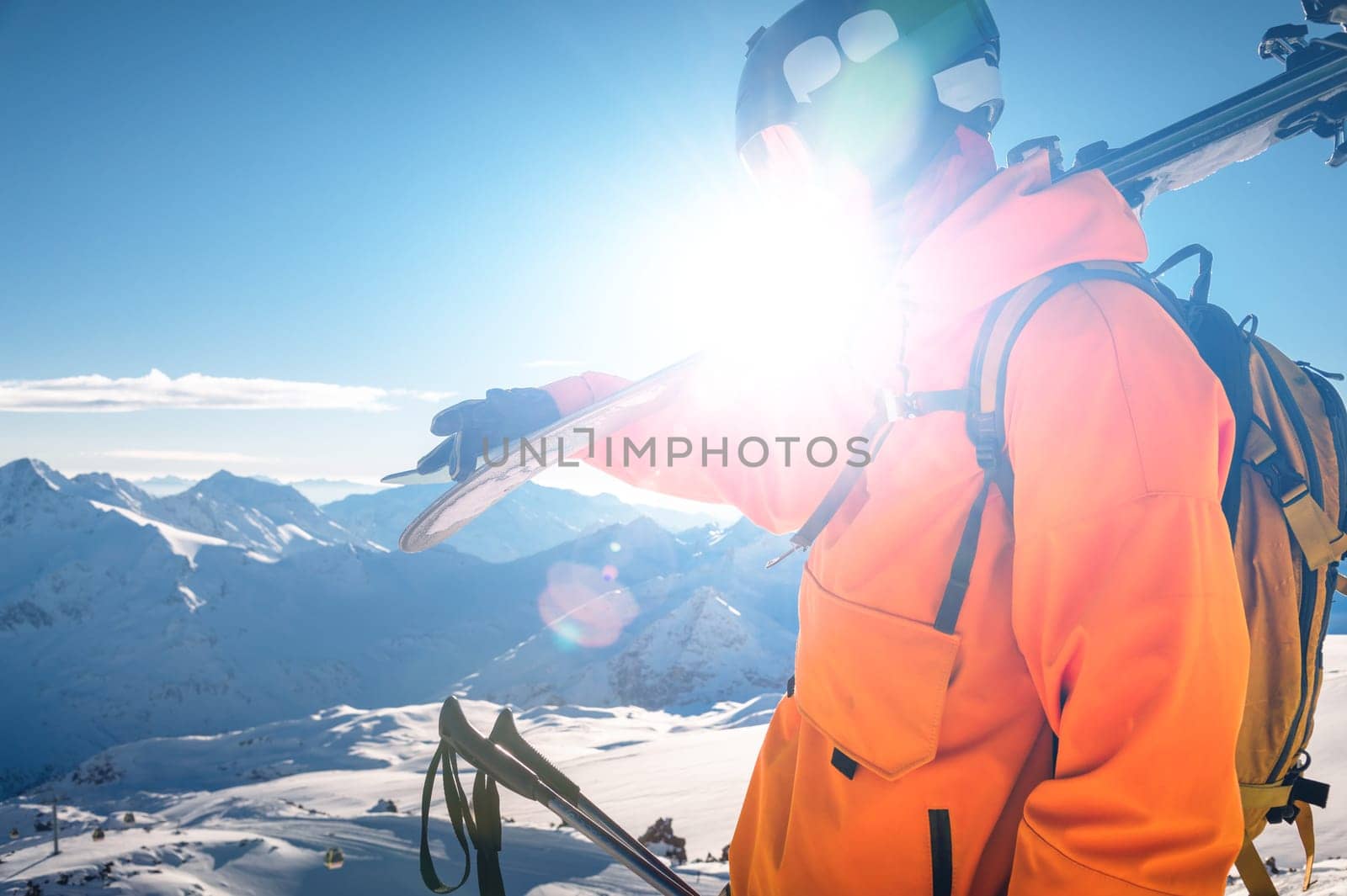 shot of a skier standing on top of a mountain with skis on his shoulder on a sunny winter day, sunlight, outdoor recreation, skiing, lifestyle, downhill sport concept by yanik88