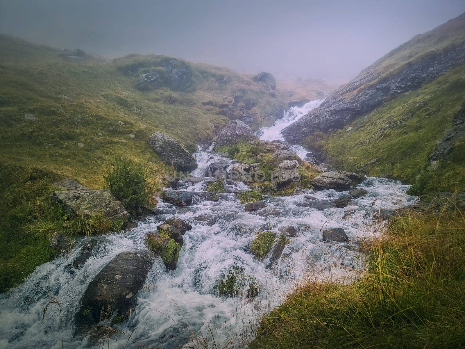 Fast stream flowing across a rocky valley in Fagaras Mountains. River with waterfalls and dense mist landscape by psychoshadow