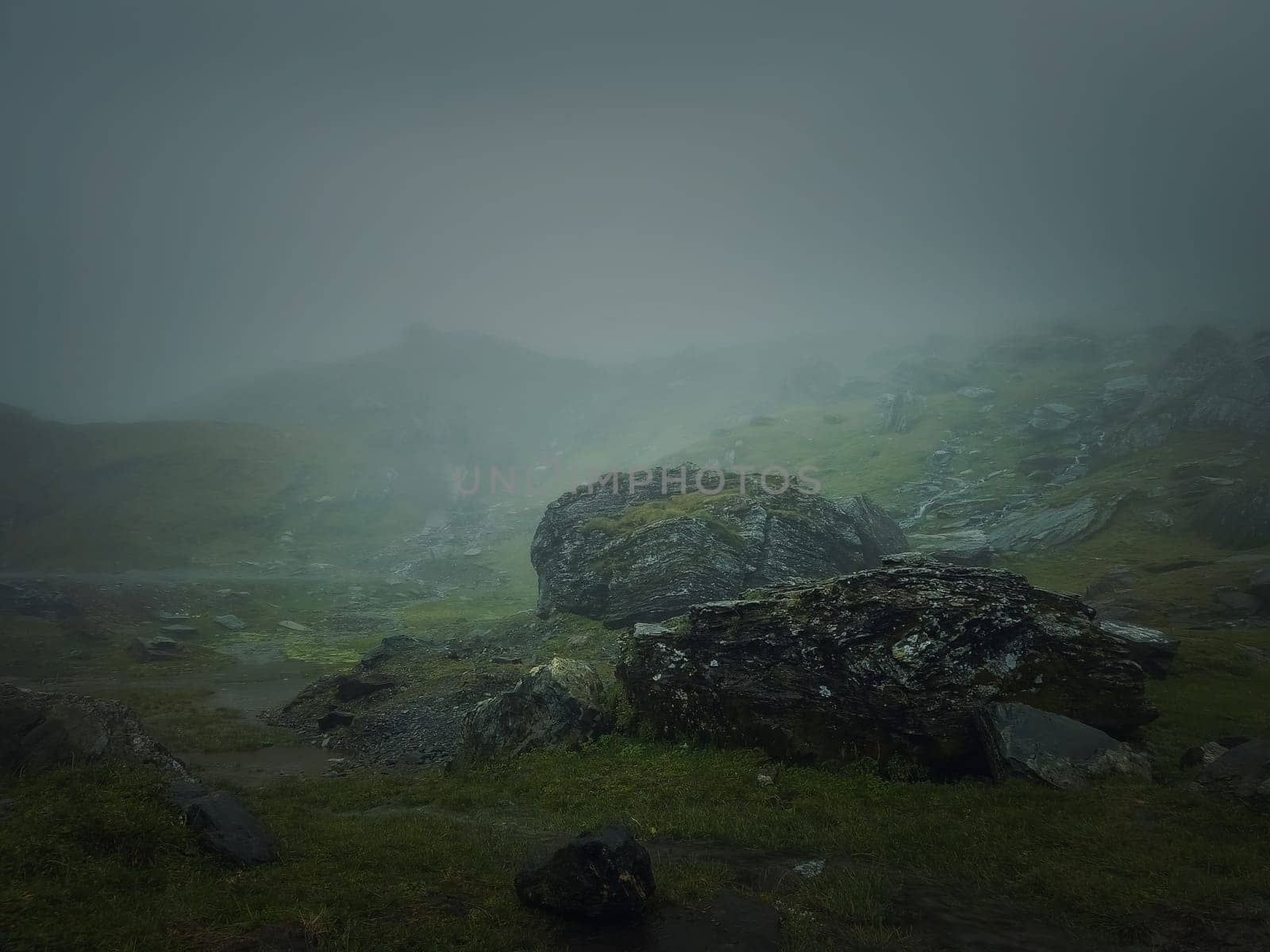 Big mountain rocks and boulders seen through the dense mist. Moody hiking scene with rainy weather by psychoshadow