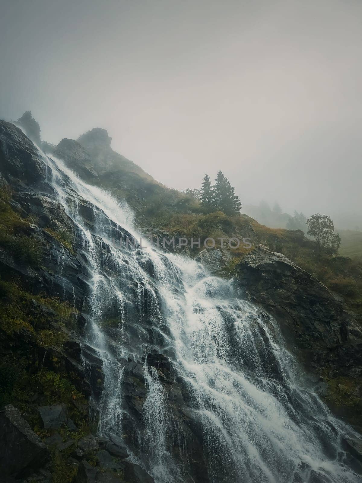 Capra waterfall on the Transfagarasan winding route of Carpathian mountains, Romania. Wonderful landscape with a tumultuous river flowing down through the cliffs in a foggy autumn morning by psychoshadow