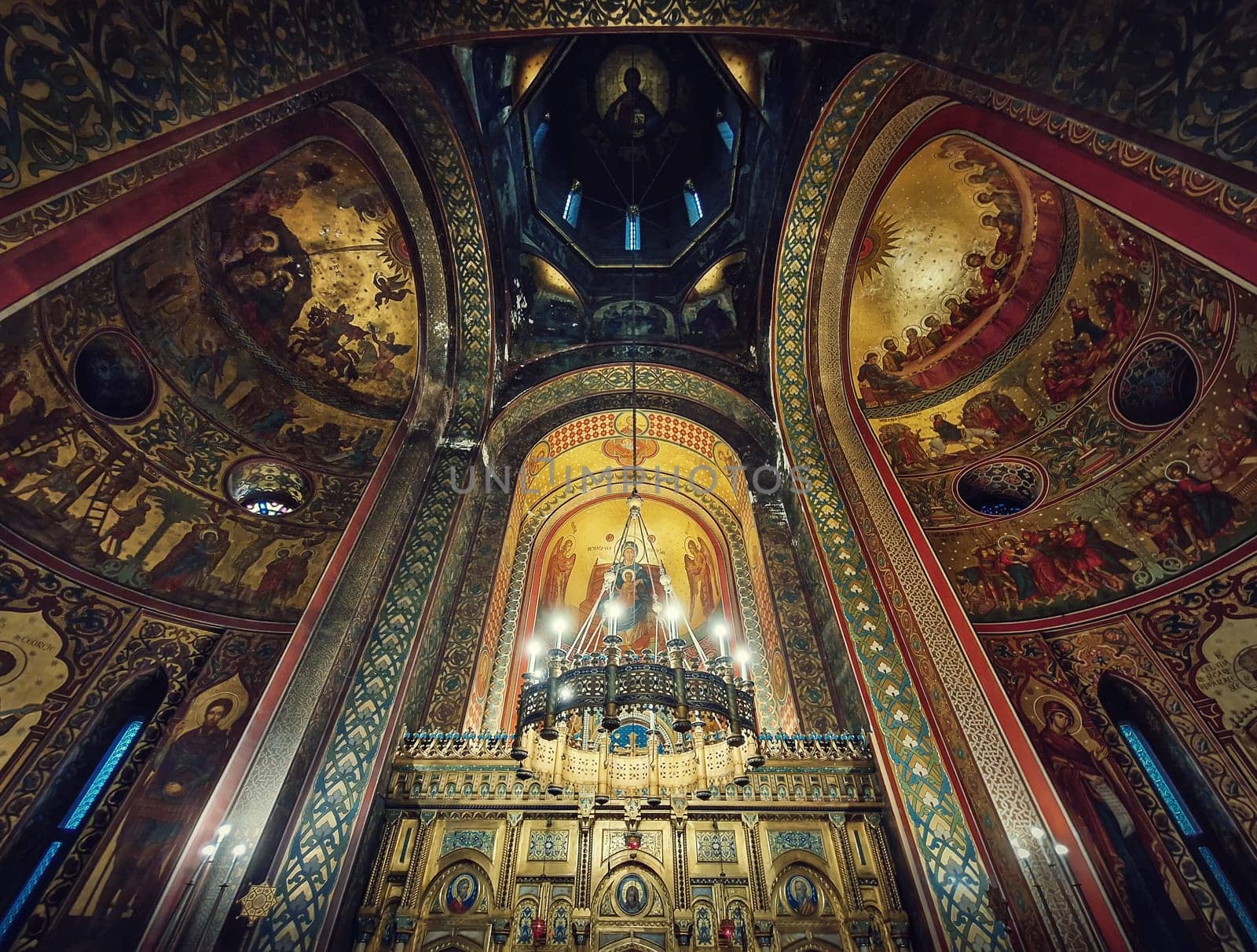 Interior architectural details of the Curtea de Arges monastery. The tall hall with painted icons, the golden altar and a chandelier with lights suspending out of ceiling
