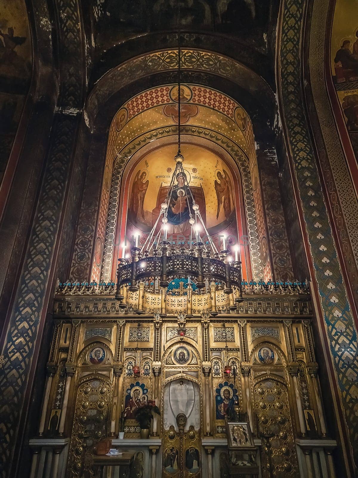 Interior details of Curtea de Arges monastery. The altar and ornate walls with painted icons and a golden chandelier with lights suspending out of ceiling