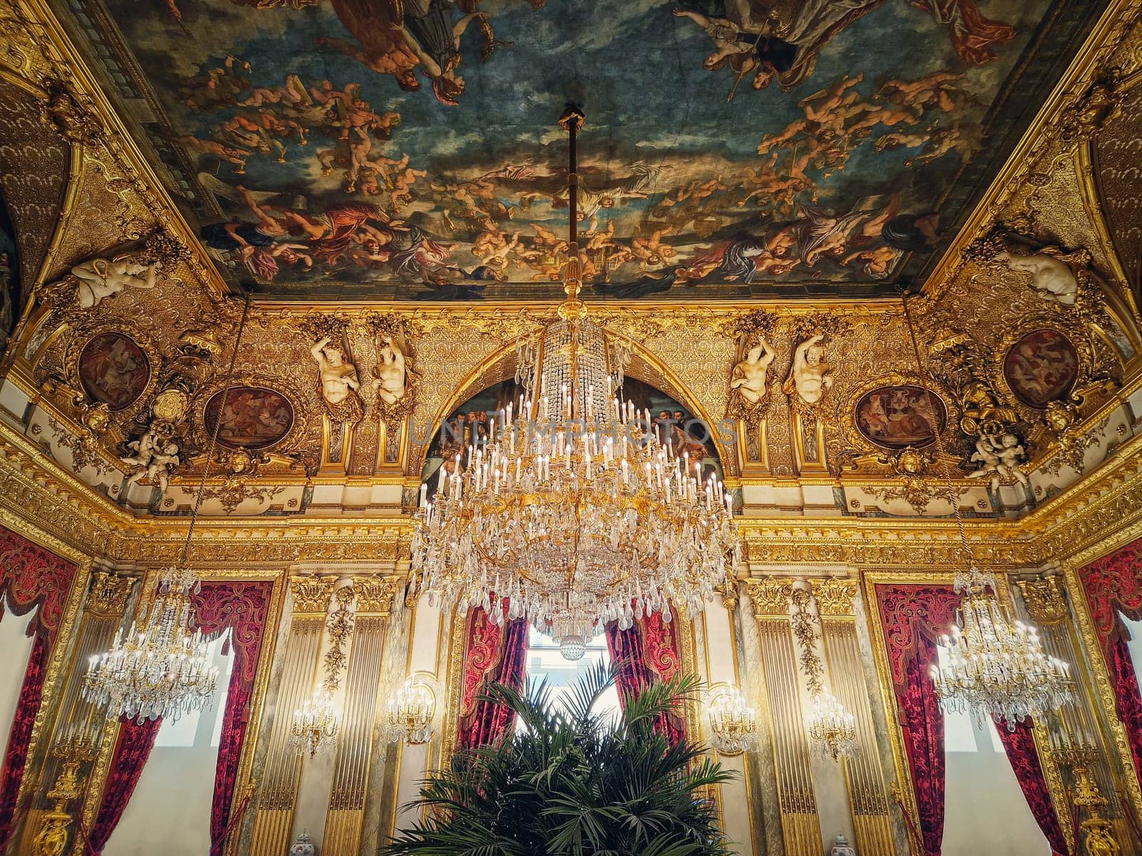 Beautiful decorated Napoleon apartments at Louvre palace. Royal family rooms with cardinal red curtains, golden ornate walls, paintings and crystal chandeliers suspended from ceiling