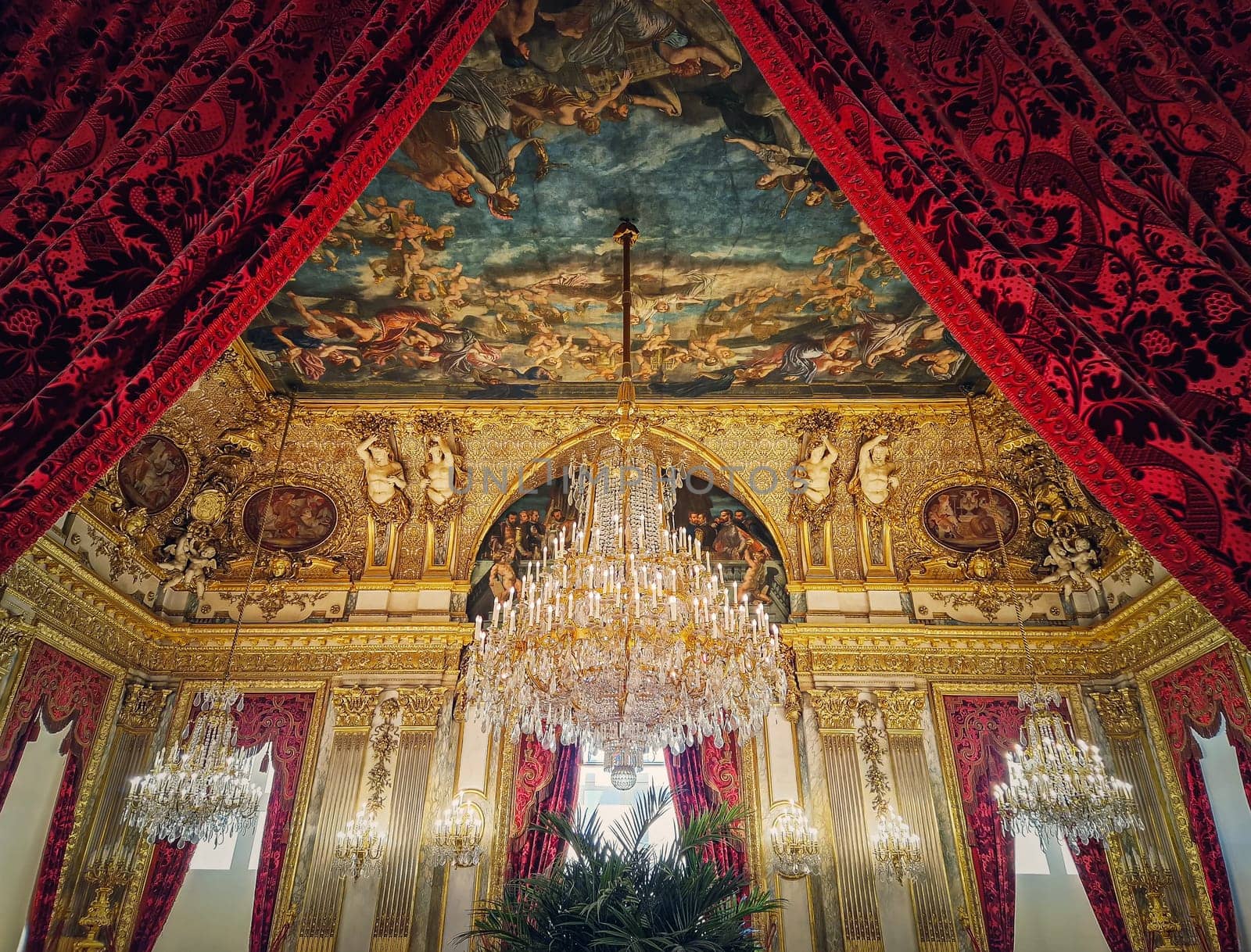 Beautiful decorated Napoleon apartments at Louvre palace. Royal family rooms with cardinal red curtains, golden ornate walls, paintings and crystal chandeliers suspended from ceiling