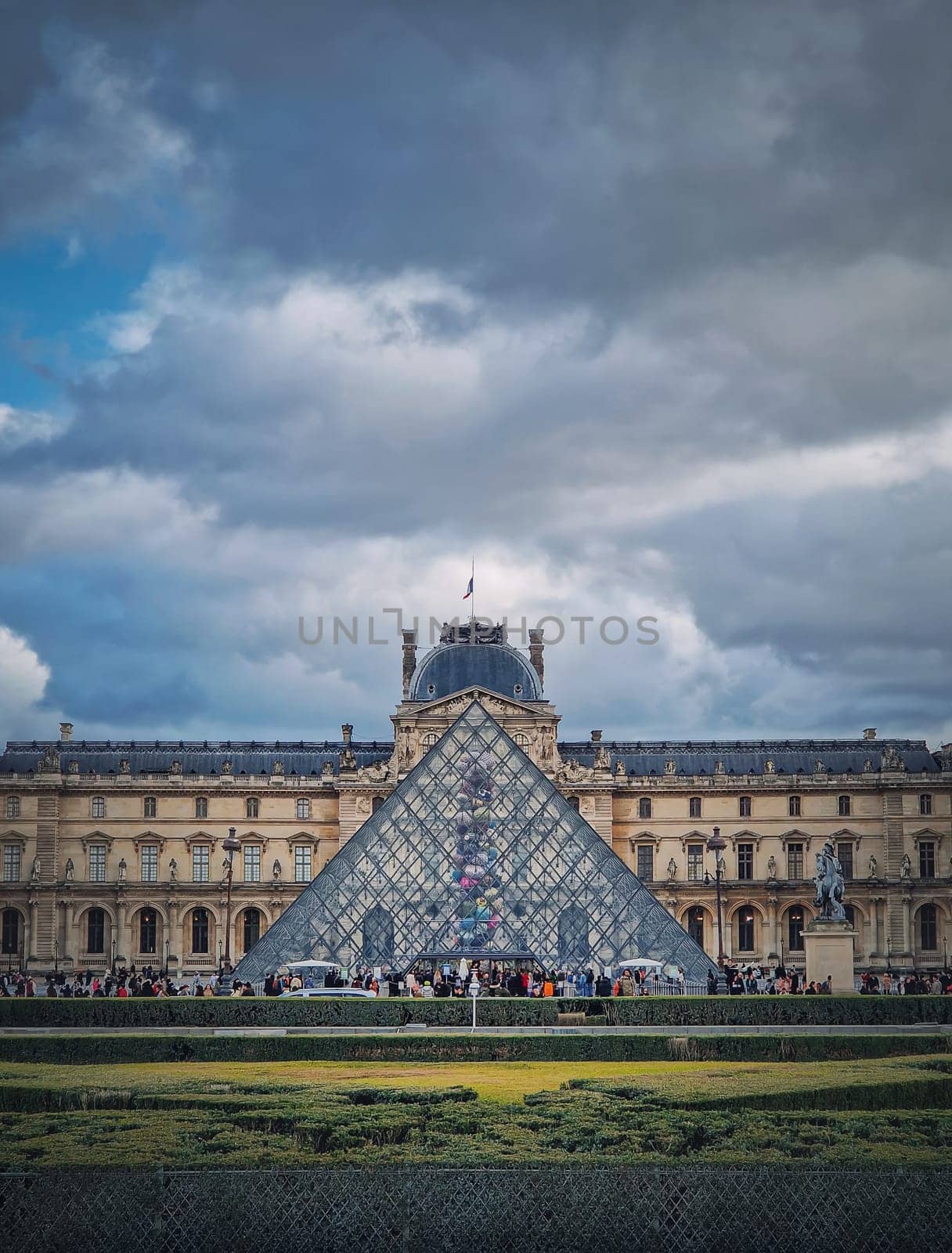 Outdoors view to the Louvre Museum in Paris, France. The historical palace building with the modern glass pyramid in center, vertical background by psychoshadow