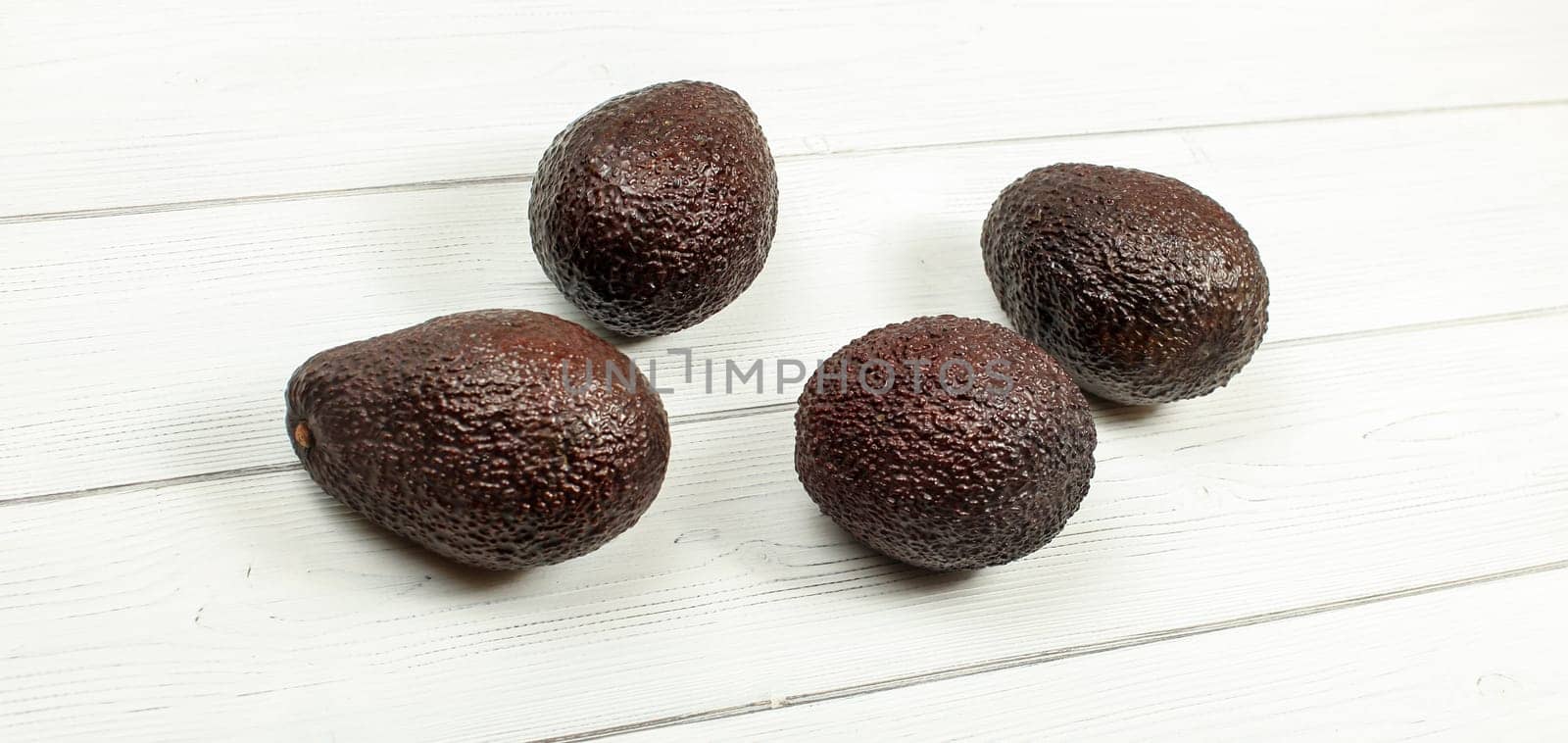 Four brown ripe avocados on white boards.